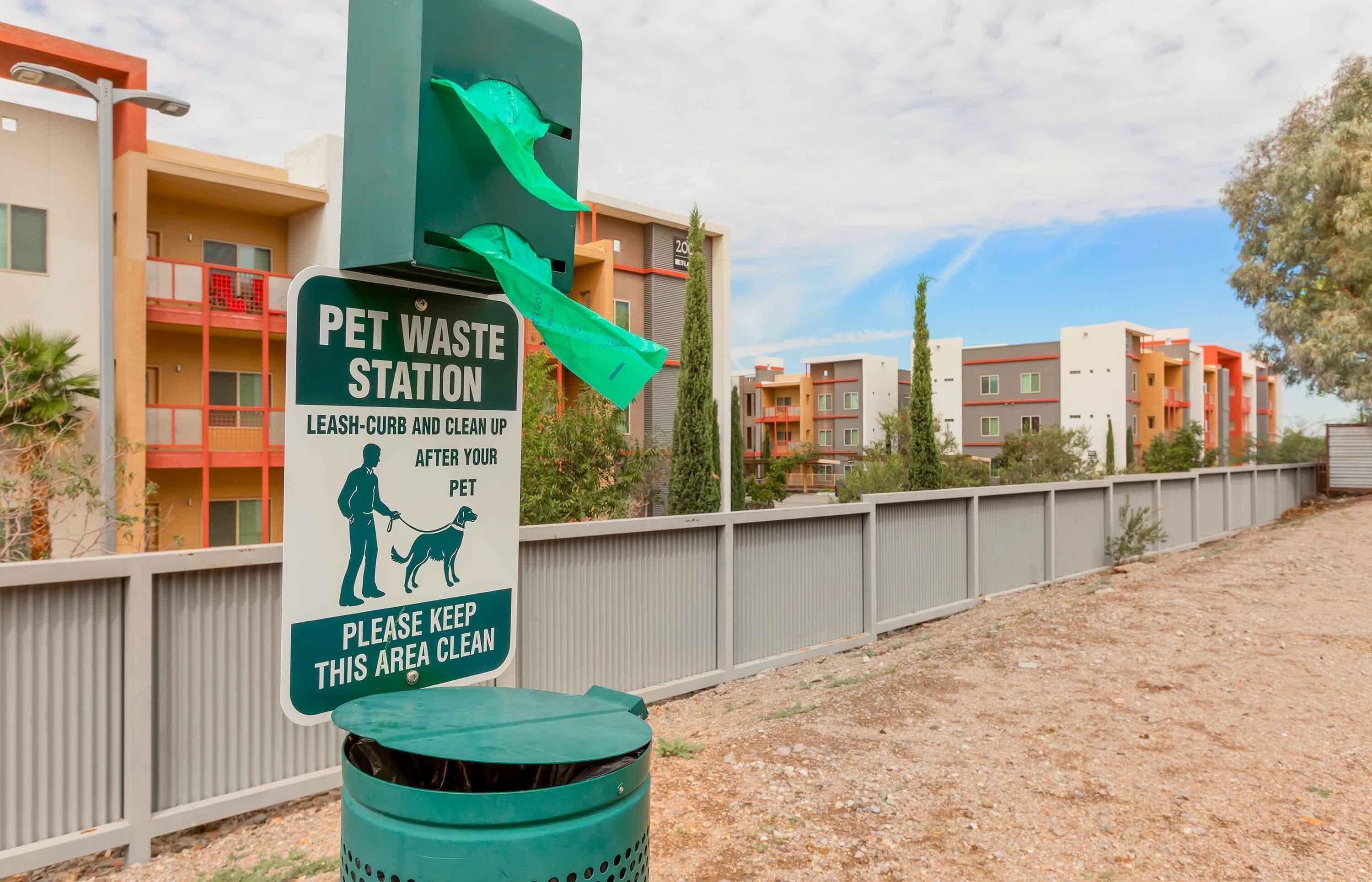 Una estación de recogida de desechos de mascotas con un cartel que indica sujetar a la mascota con correa y limpiar después de ella.