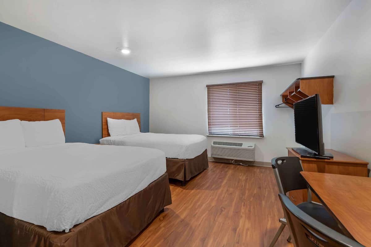 Habitación de hotel con dos camas, un escritorio, una silla, un televisor y una ventana con persianas.