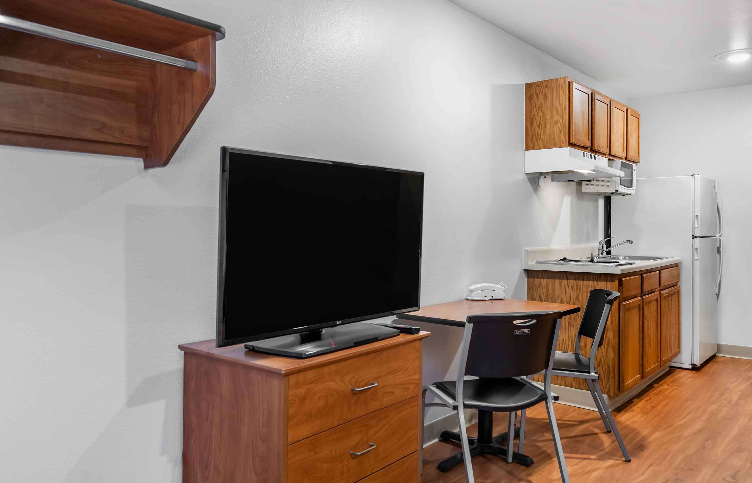 A compact kitchenette with a flat-screen TV, wooden cabinets, a microwave, and a refrigerator.