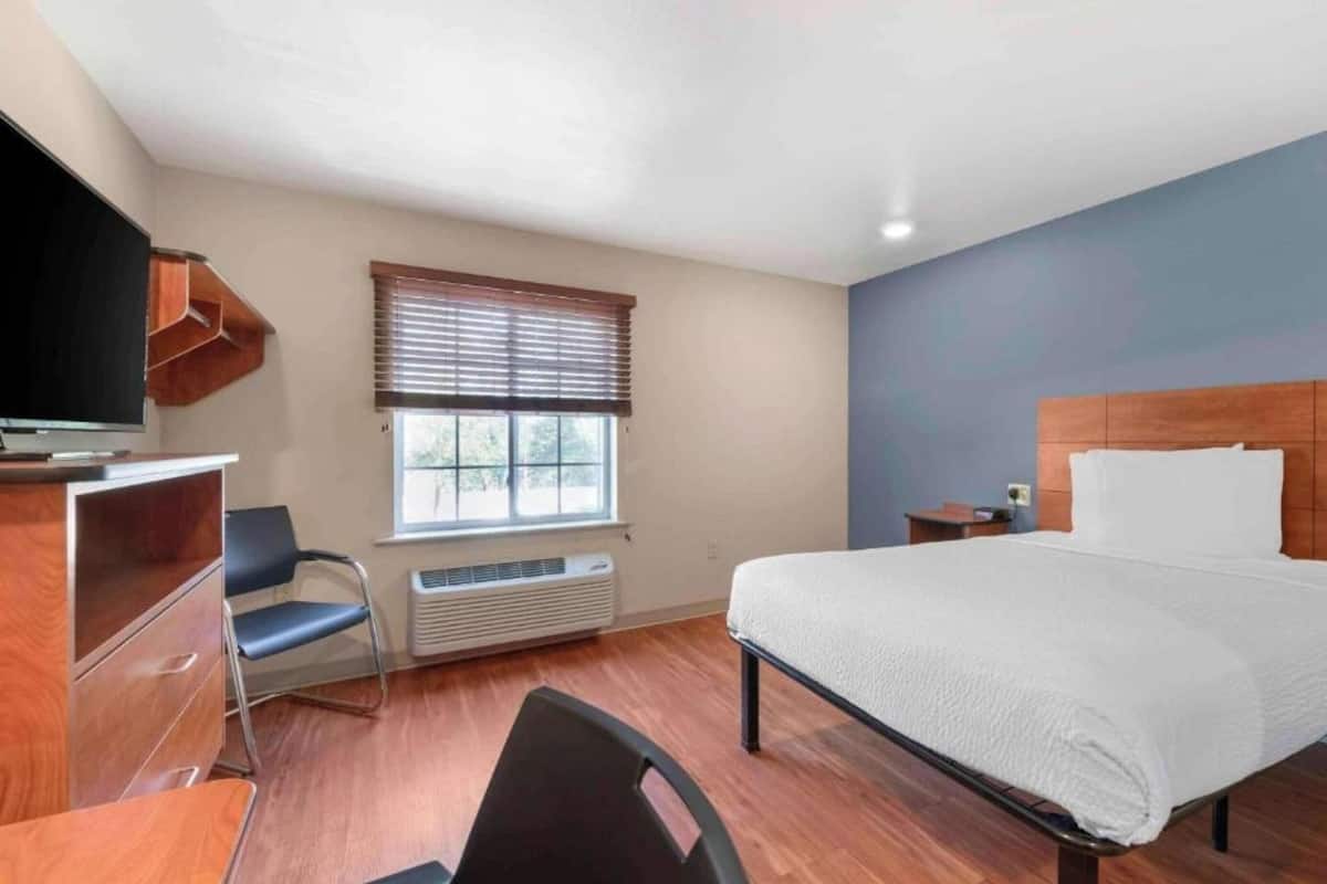 Une chambre d’hôtel équipée d’un lit, d’un bureau, d’une chaise, d’une télévision, d’une fenêtre avec des stores et d’un radiateur.