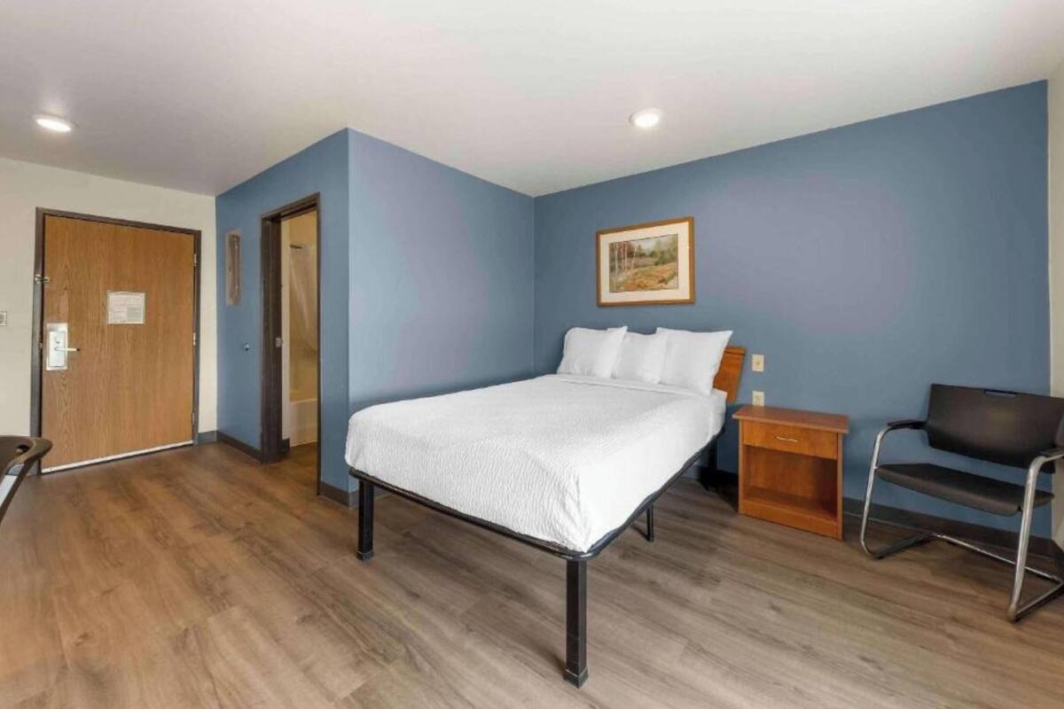 Une pièce comprenant un lit, une chaise, une table de chevet en bois et une porte.