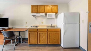Cocina compacta con armarios de madera, microondas, refrigerador y comedor con una silla y mesa.