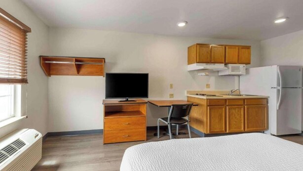 Habitación compacta con cama, escritorio, silla, televisor, armarios de madera, microondas y refrigerador.