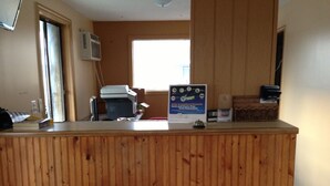 Un comptoir d’accueil avec un revêtement en bois, une fenêtre avec des stores, un climatiseur fixé au mur et un panneau d’affichage indiquant les récompenses.