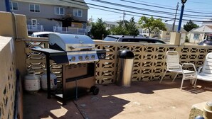 Un espace extérieur aménagé en patio, avec un barbecue, une poubelle et une chaise blanche.