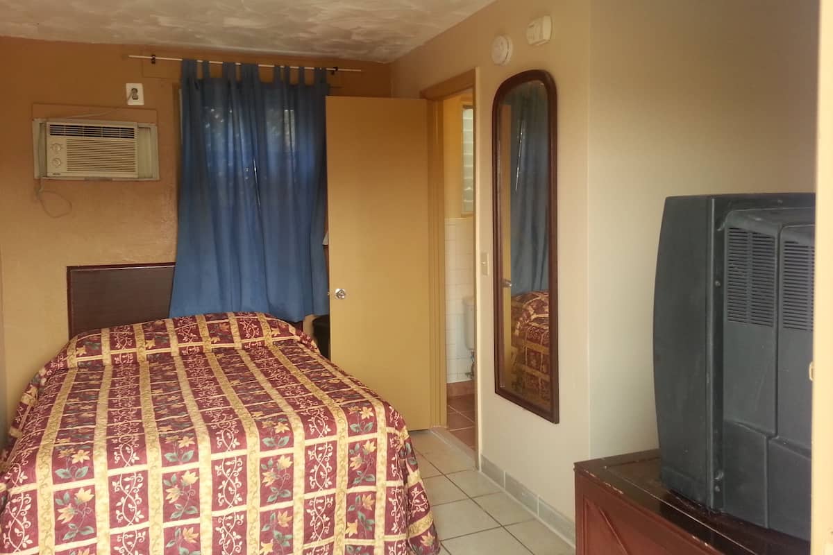 A bedroom with a bed, a television, a mirror, and a window with curtains.