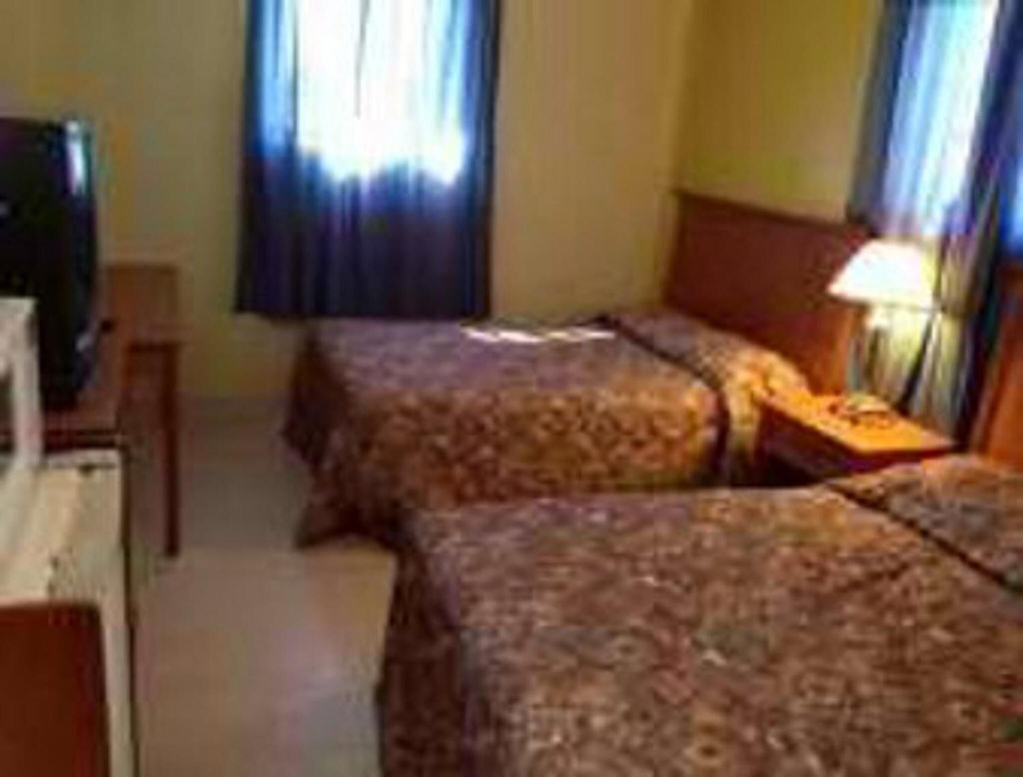 A hotel room with two beds, a TV, and a lamp.