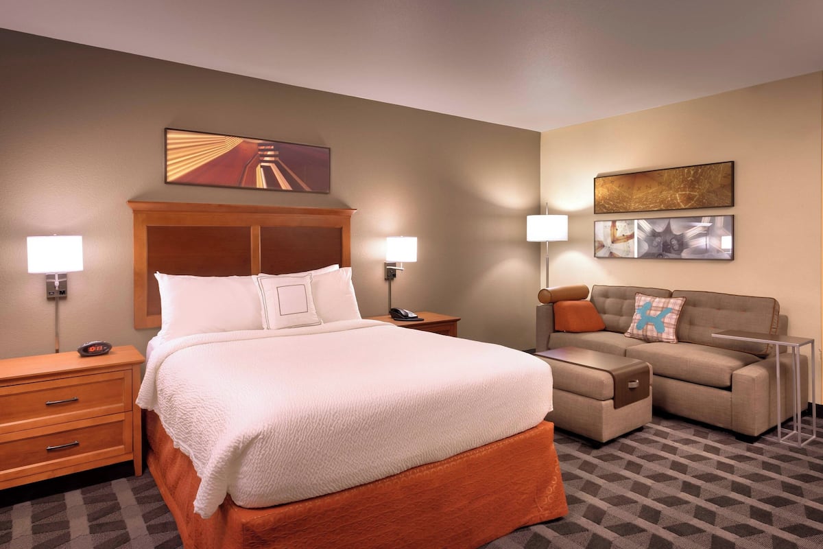 A hotel room with a large bed, a sofa, a nightstand, and two wall-mounted lamps.