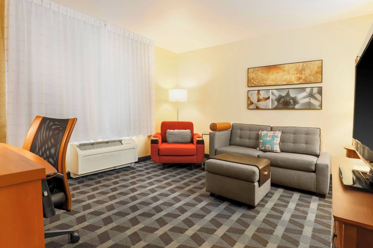 A hotel room with a sofa, armchair, ottoman, desk, and a flat-screen TV.