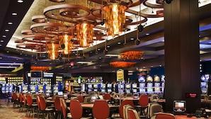 Un casino doté de nombreuses tables de jeu et de chaises, d’un grand lustre et de machines à sous en arrière-plan.