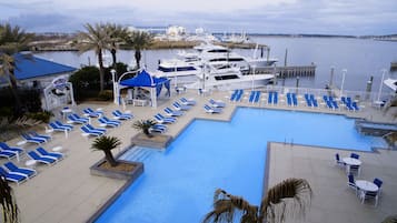 Relax by the marina's tranquil pool, surrounded by lounge chairs and umbrellas, with yachts docked in the distance.