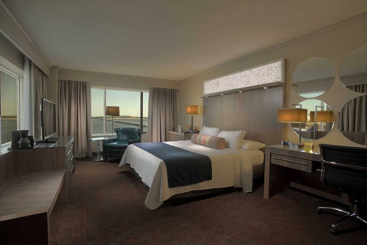 Een hotelkamer met een groot bed, een bureau, een stoel, een bureaulamp, een nachtkastje en een raam met gordijnen.