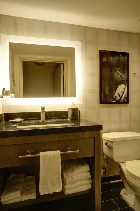 Un baño con lavamanos, espejo, toallero y retrete.