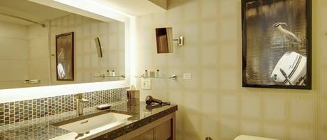 A bathroom with a large mirror, a sink, a toilet, and a framed picture of a bird on a boat.
