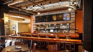 A bar area with wooden bar counters, stools, and a variety of bottles and glasses. - Craddock Terry Hotel, Lynchburg, a Tribute Portfolio Hotel (Lynchburg)