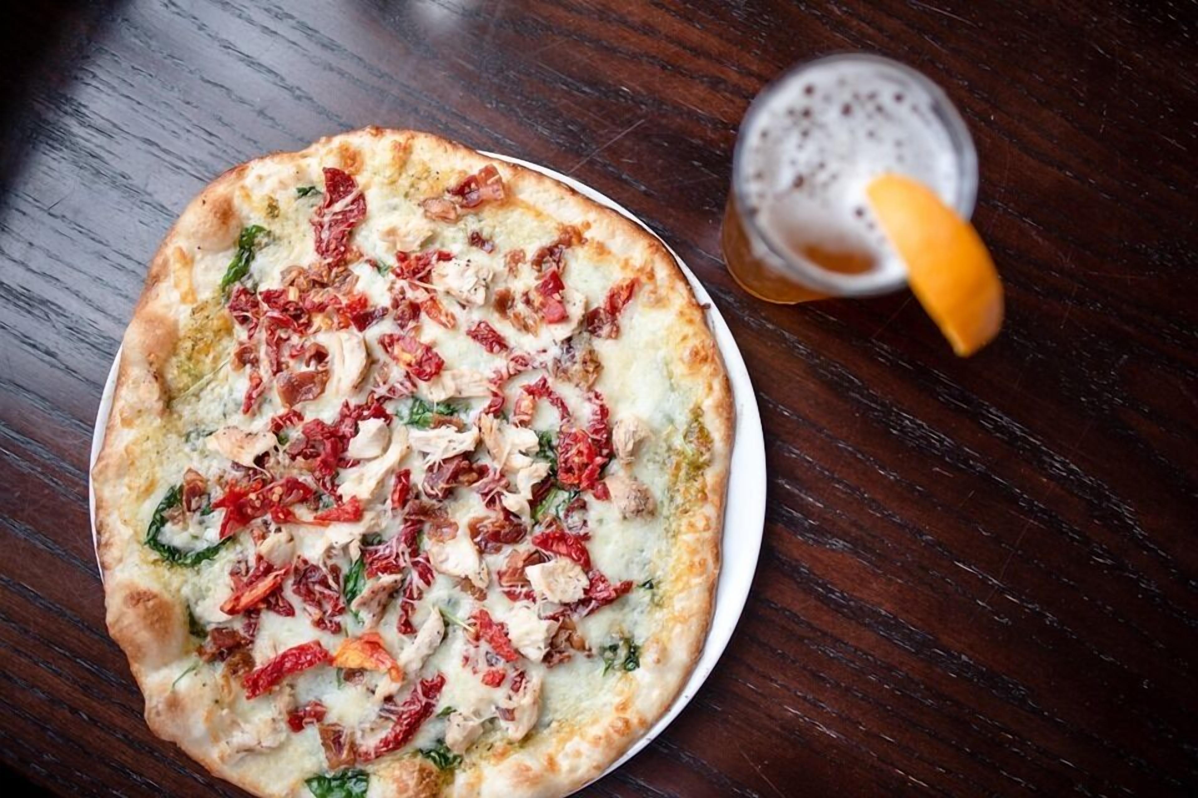 A pizza with toppings on a white plate, accompanied by a glass of a beverage with a lemon wedge.