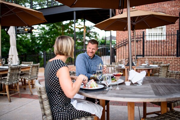 An outdoor dining area with tables and chairs, umbrellas, and a brick building in the background. - Craddock Terry Hotel, Lynchburg, a Tribute Portfolio Hotel (Lynchburg)