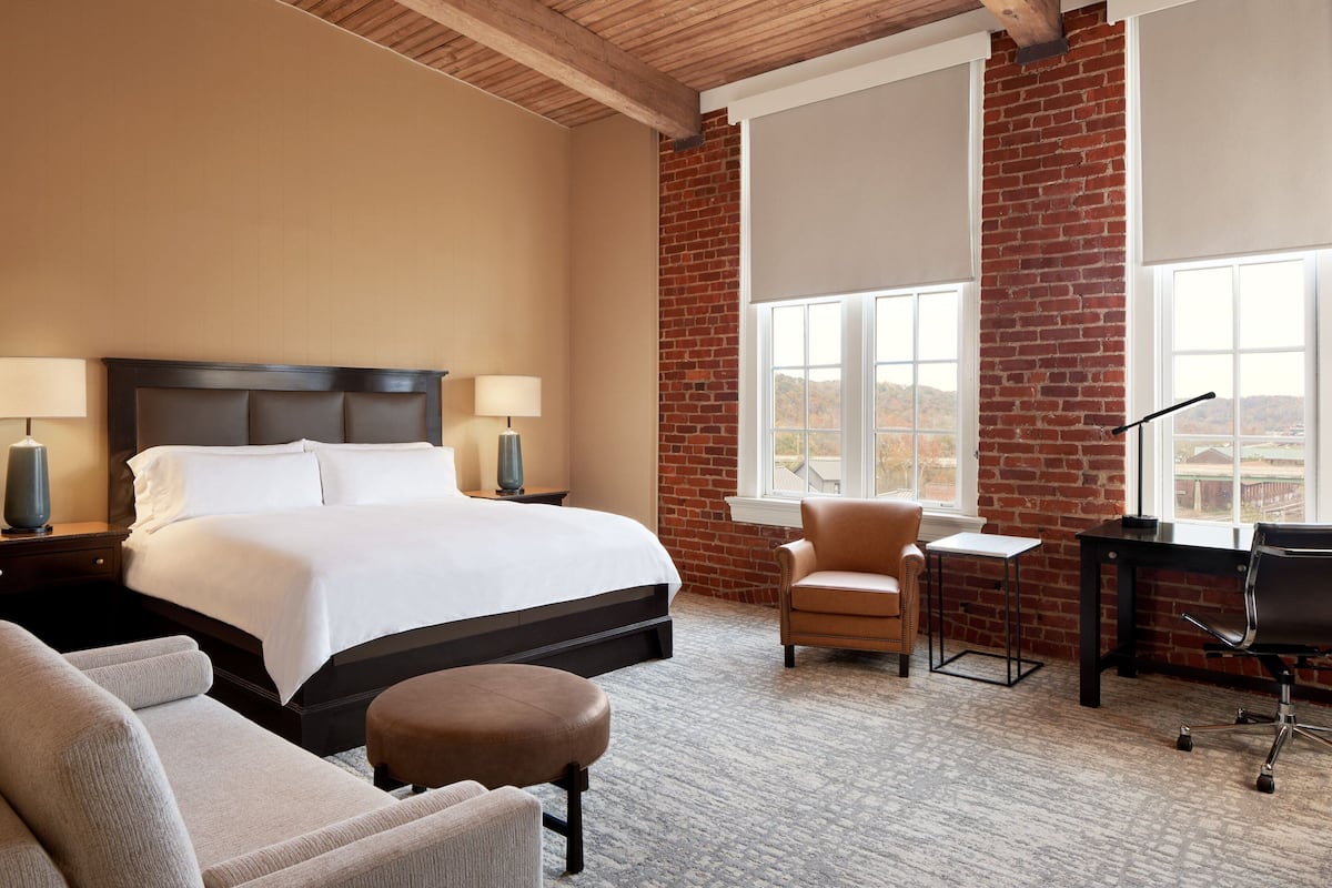 A hotel room with a large bed, a desk, a chair, and a view of the outside.