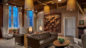 A cozy living room with a leather sofa, armchairs, and a coffee table. There are pendant lights, a shoe display wall, and a fireplace. - Craddock Terry Hotel, Lynchburg, a Tribute Portfolio Hotel (Lynchburg)