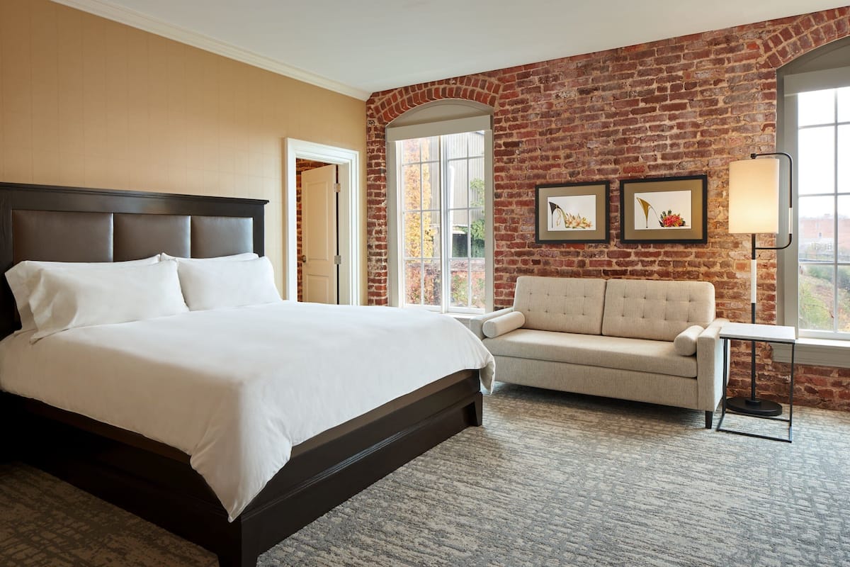 A hotel room with a large bed, a sofa, a small table, and a brick wall.