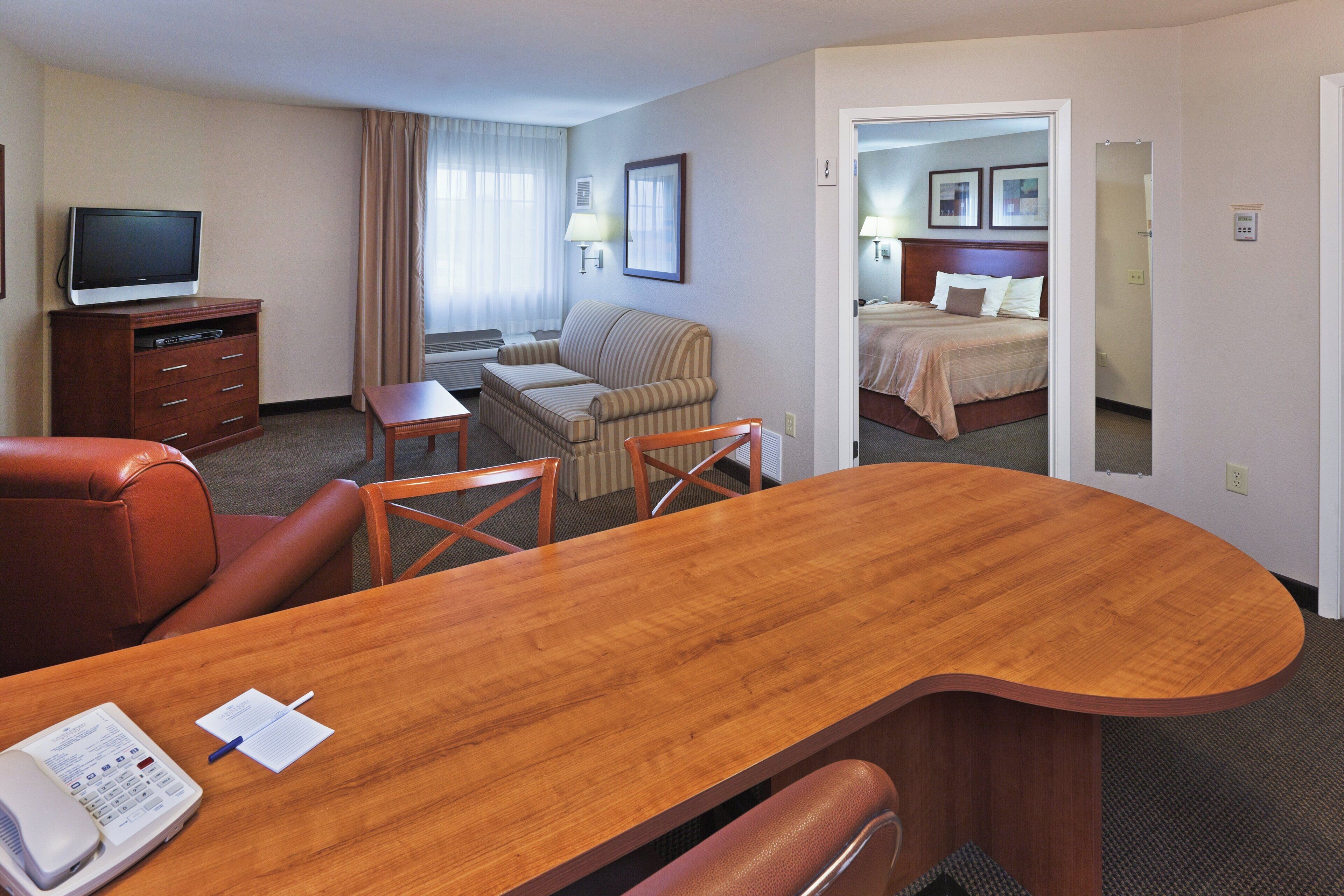 Quarto de hotel com escrivaninha de madeira, poltrona de couro, televisão, sofá e cama.