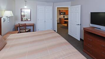 A hotel room with a bed, a desk, a chair, a television, and a kitchenette in the background.