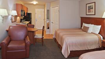 A hotel room with a bed, a desk with a chair, a television, and a kitchenette.