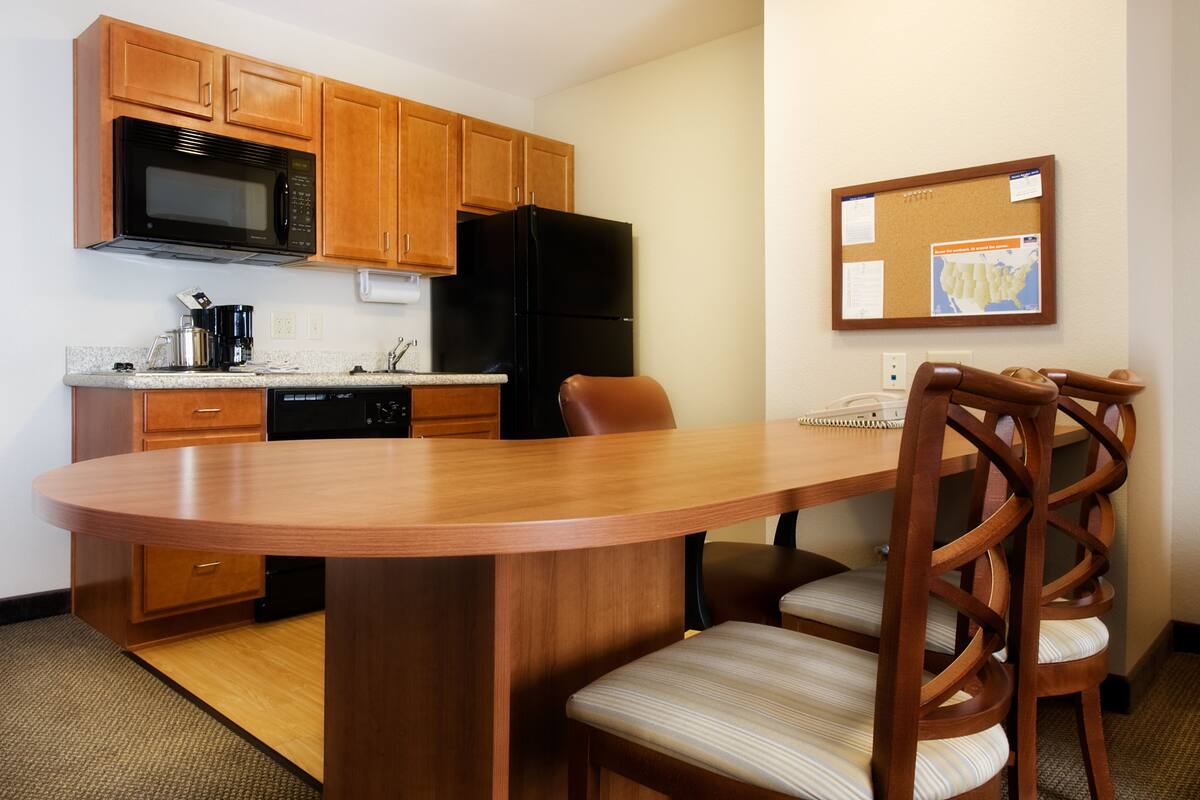 Una cocina compacta con armarios de madera, un refrigerador negro, un microondas y una zona de comedor con mesa y sillas de madera.