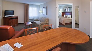 Habitación de hotel con un escritorio de madera, una butaca de cuero, un sofá, un televisor y una cama con cabecera.