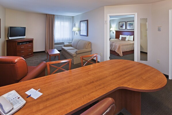 Habitación de hotel con un escritorio de madera, una butaca de cuero, un sofá, un televisor y una cama con cabecera.