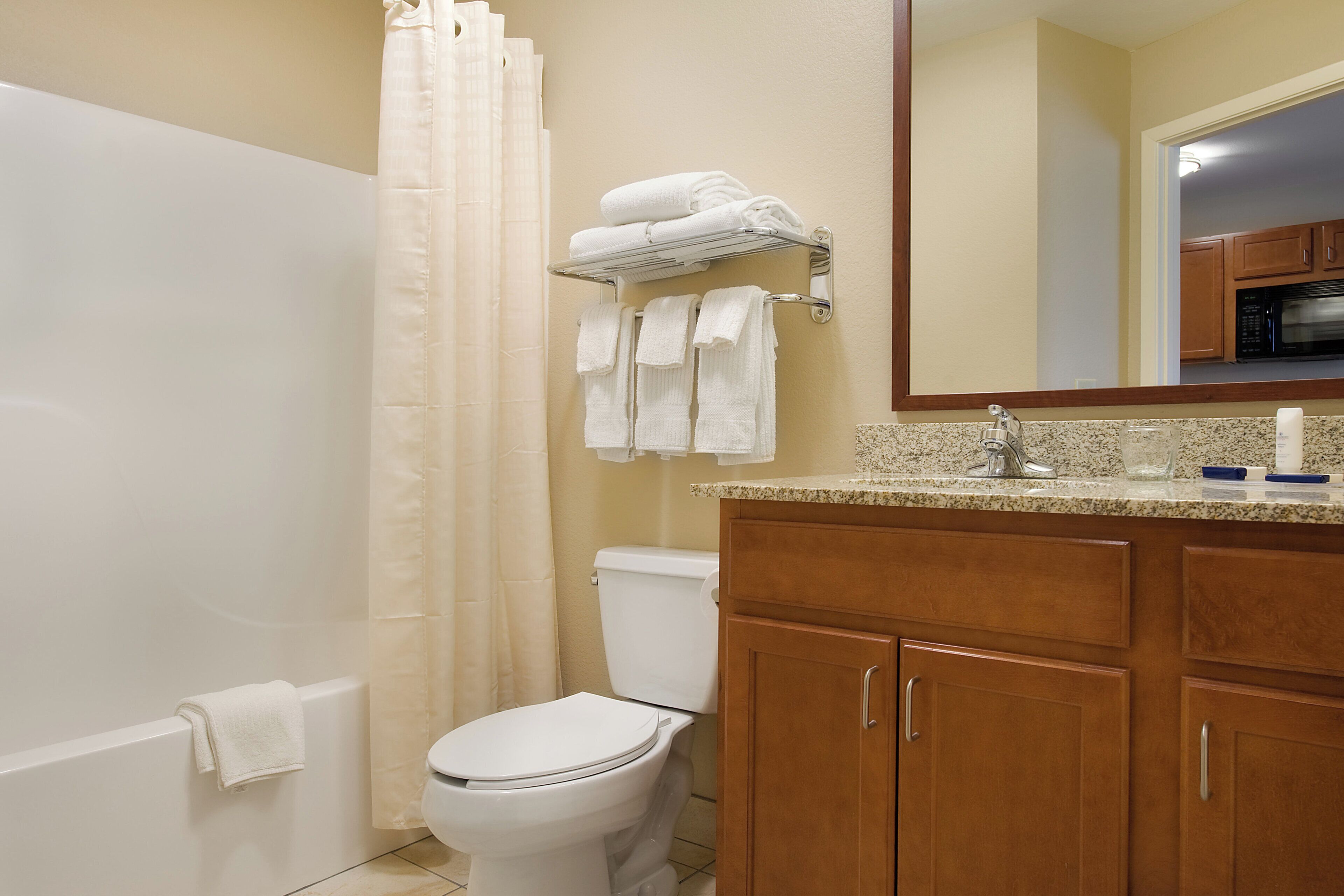 Une salle de bain comprenant des toilettes, un rideau de douche, un porte-serviettes avec des serviettes, un lavabo avec un miroir et des meubles en bois.