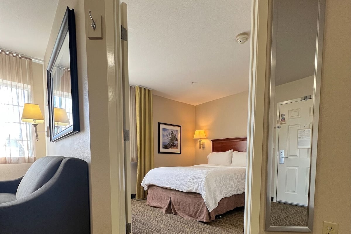 Habitación de hotel con cama, escritorio, silla, lámpara y espejo.