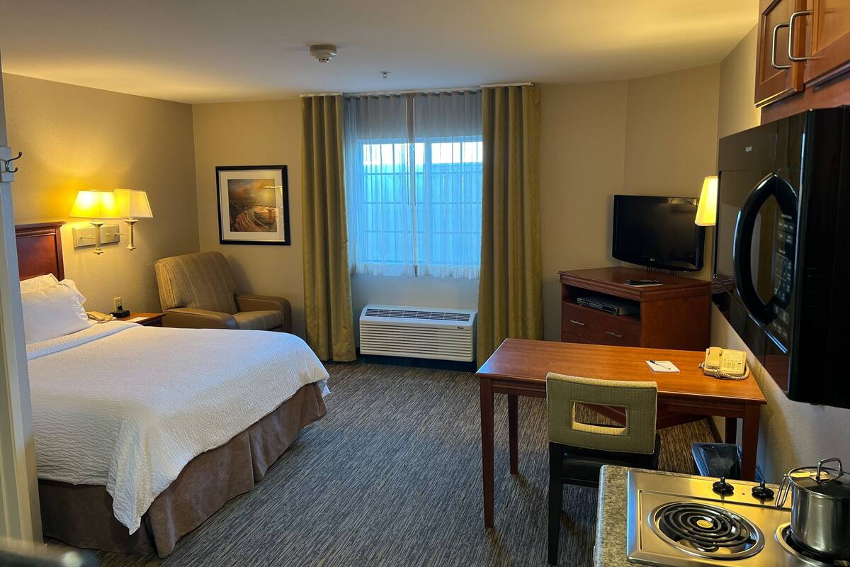 Habitación de hotel con cama, escritorio, televisor, microondas y ventana con cortinas.