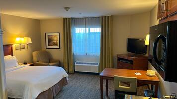 A hotel room with a bed, a desk, a television, a microwave, and a window with curtains.