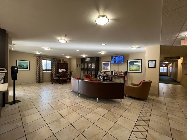Un vestíbul d'hotel amb una recepció, zona de seients i un televisor penjat a la paret.