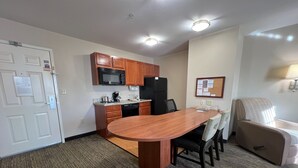 Una habitación de hotel con una mesa de comedor, sillas, microondas, refrigerador y una peque ña kitchenette.