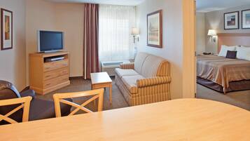 A hotel room with a television on a wooden cabinet, a sofa, a small table, and a bed with a headboard.
