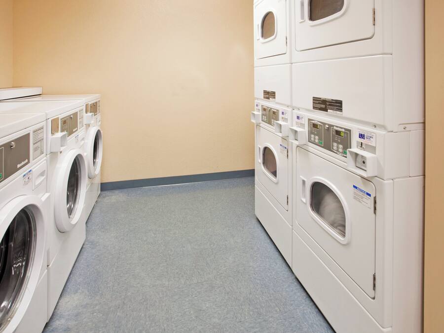 A laundry room with multiple washing machines and dryers, a grey floor, and beige walls.