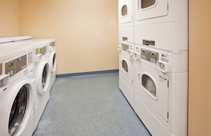 A laundry room with multiple washing machines and dryers, a grey floor, and beige walls.