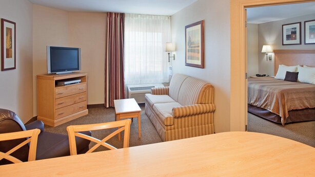 Ein Hotelzimmer mit Fernseher auf einer Holzkommode, einer Couch, einem kleinen Tisch und einem Bett mit Kopfteil.