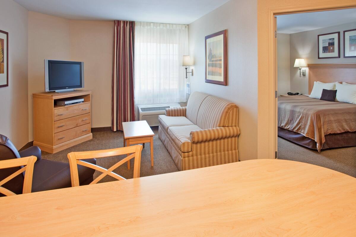 Habitación de hotel con televisión sobre un mueble de madera, un sofá, una mesita y una cama con cabecera.