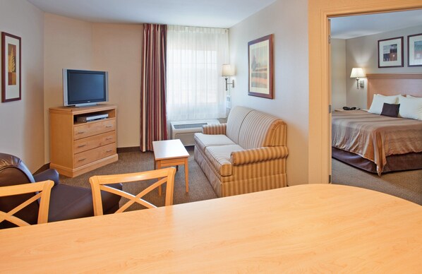 A hotel room with a television on a wooden cabinet, a sofa, a small table, and a bed with a headboard.