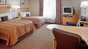 Ein Hotelzimmer mit zwei Betten, einem Schreibtisch, einem Stuhl, einem Fernseher und einem Fenster mit Vorhängen.