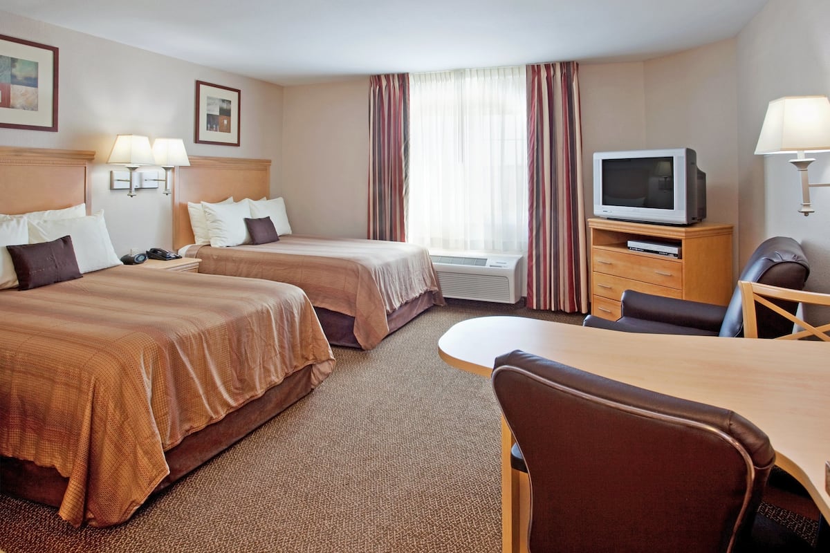 Habitación de hotel con dos camas, un escritorio, una silla, un televisor y una ventana con cortinas.