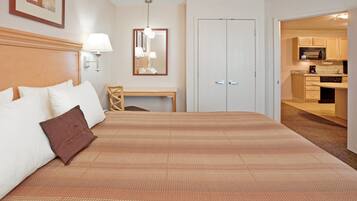Quarto de hotel com cama grande, escrivaninha, espelho e cozinha compacta.