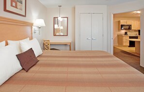 A hotel room with a large bed, a desk, a mirror, and a kitchenette.