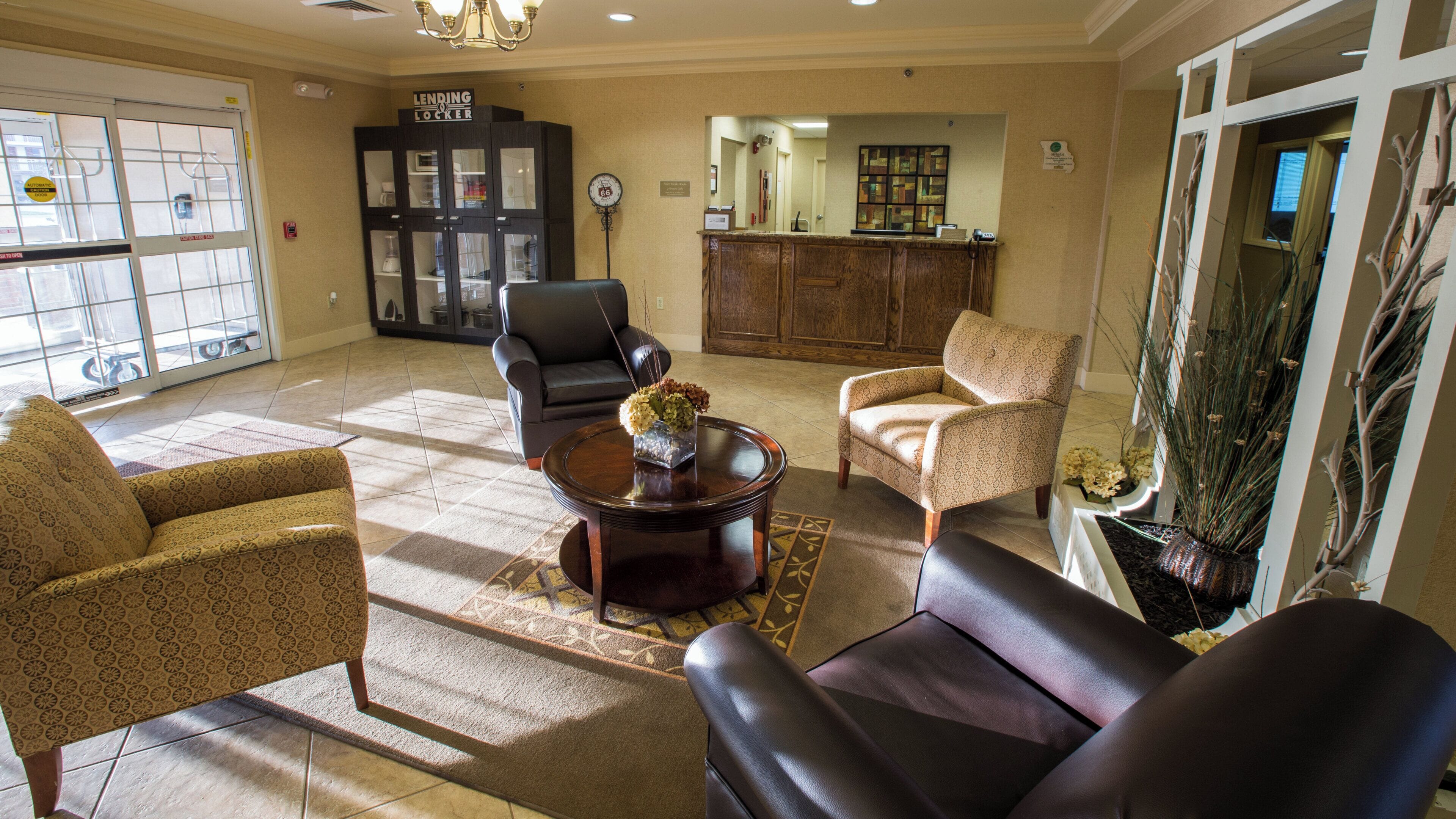 A spacious living room with a fireplace, leather armchairs, a coffee table with a vase, and a view through a large window.