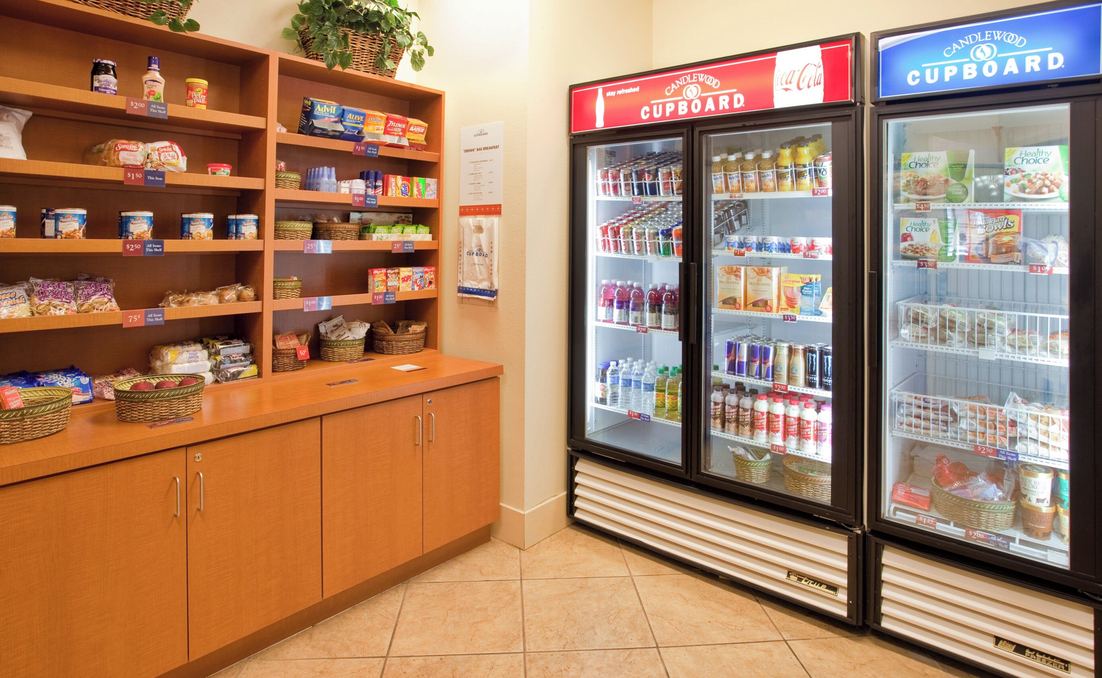 A kitchenette area with shelves stocked with various food items and two beverage dispensers labeled 'Candlewood Cupboard.'