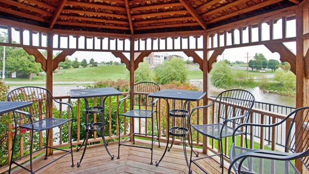 A covered outdoor seating area with tables and chairs, overlooking a river and greenery. - Candlewood Suites Springfield by IHG (Springfield)