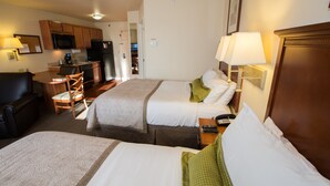 A hotel room with two beds, a desk, a chair, a kitchenette, and a bathroom.